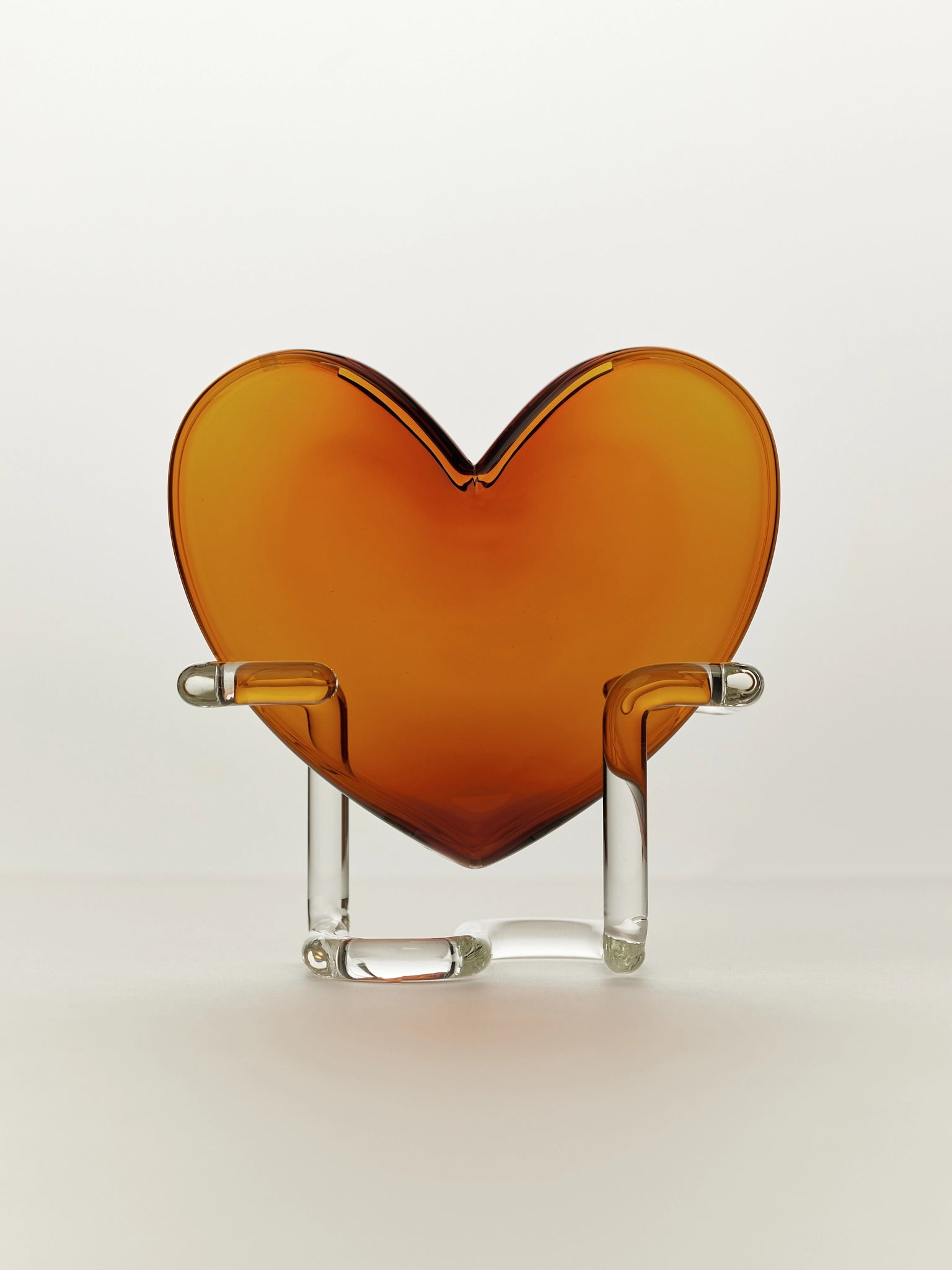 Heart-shaped amber glass vase on a clear stand against a white background