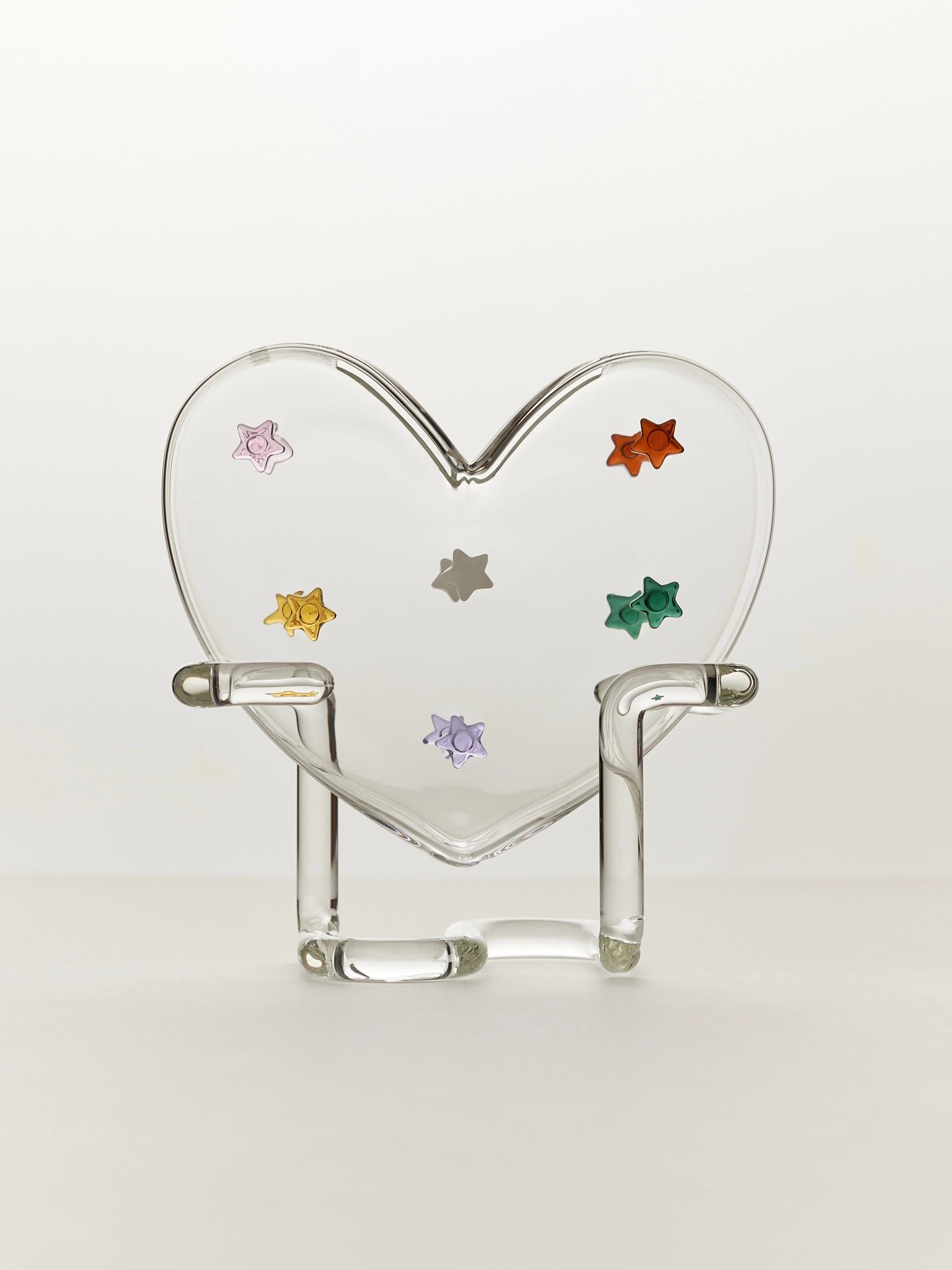 Heart-shaped glass vase with colourful stars on a clear glass stand on a white background