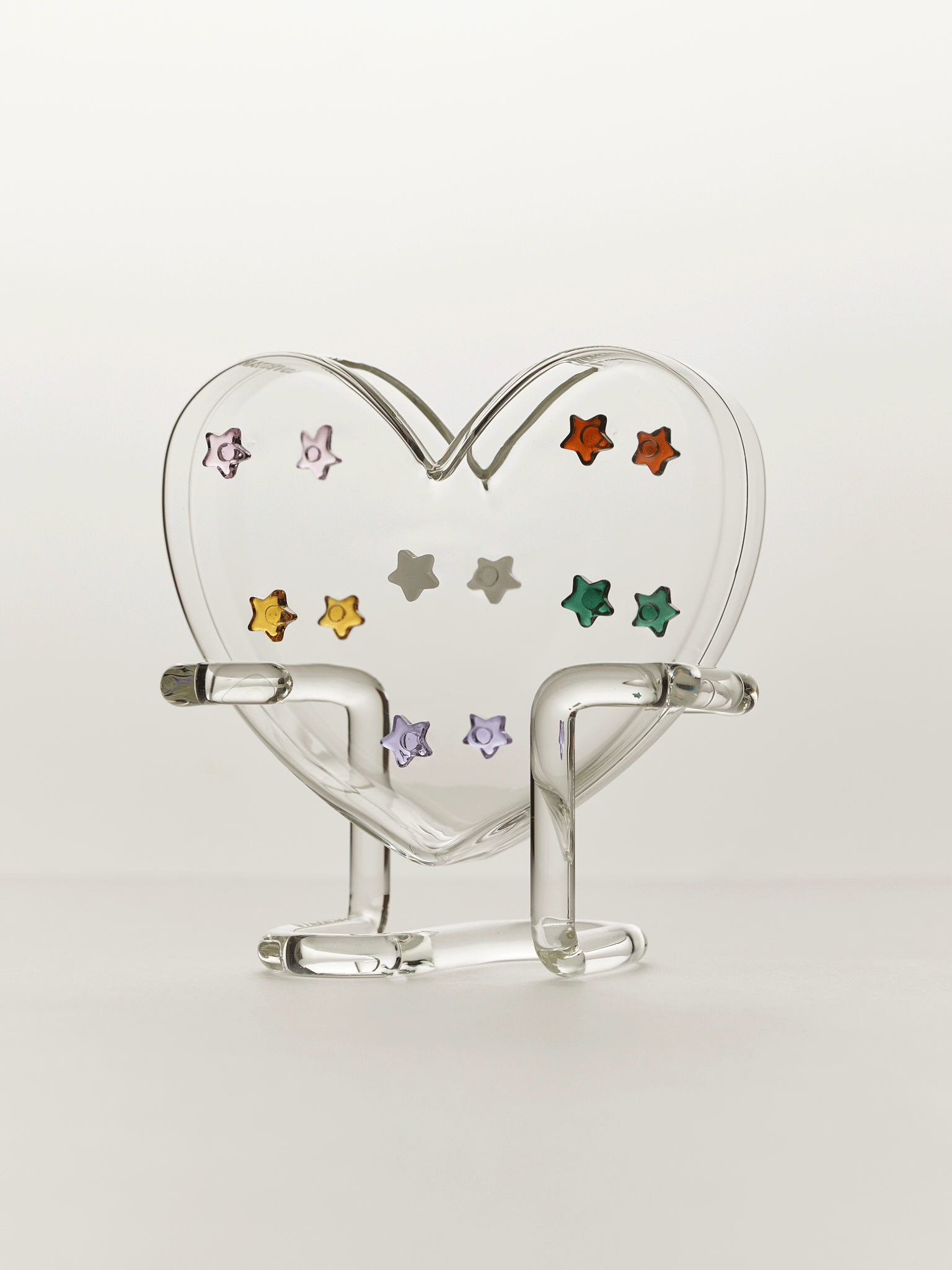 heart shaped glass vase with colourful stars on a clear base against a white background
