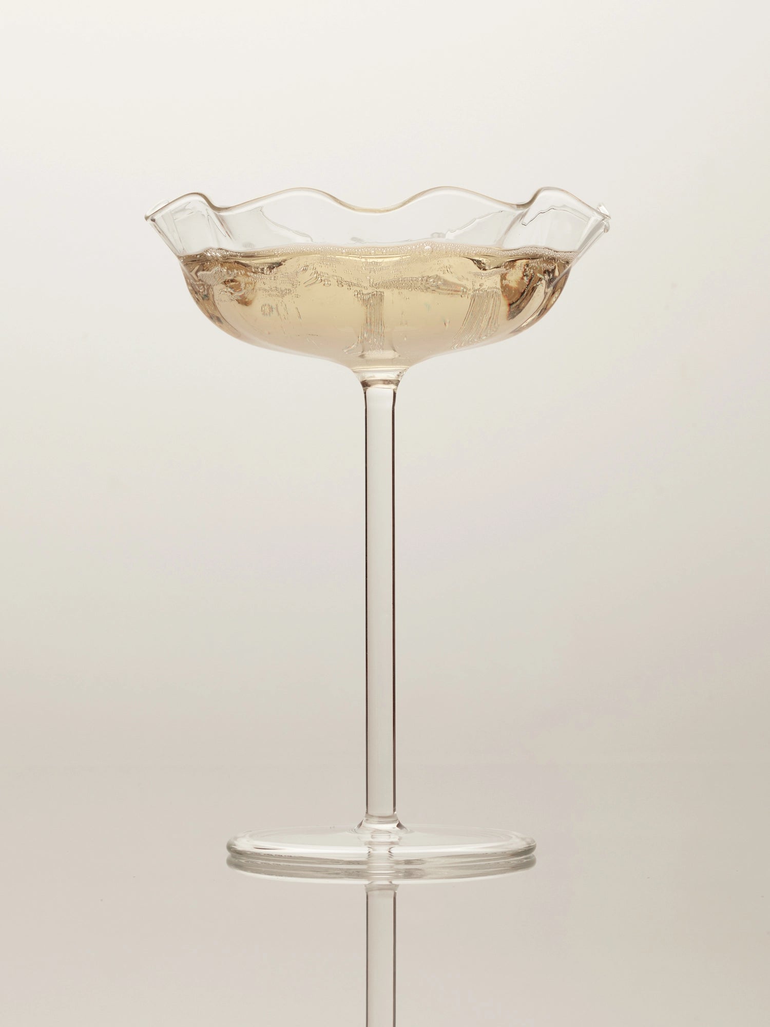 Clear champagne glass in the shape of a clam shell filled with champagne on a white background